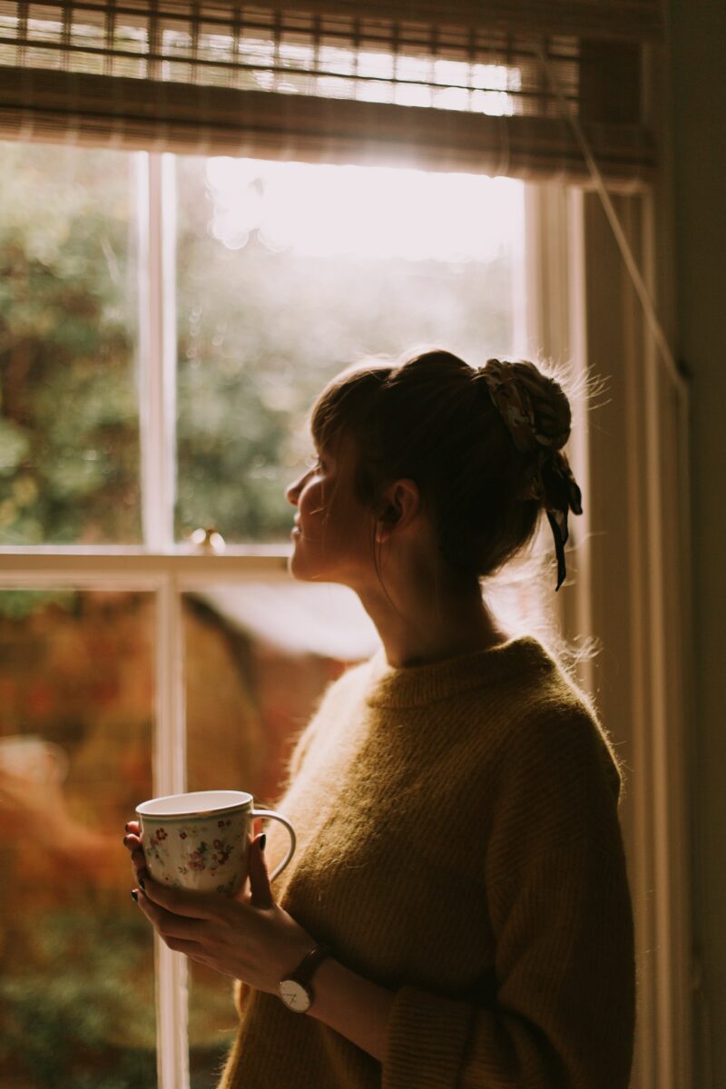 woman with coffee cup staring out sunny window