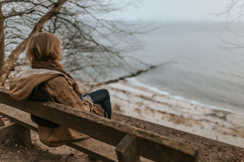 Woman sitting on bench overlooking the ocean in winter